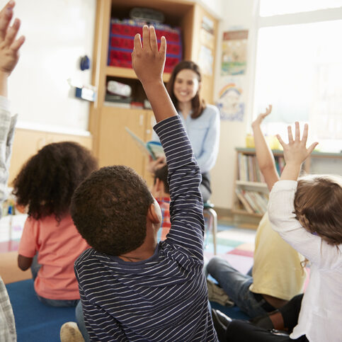 Elementary school kids raising hands to teacher, back view